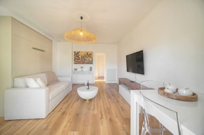 Ein modernes Wohnzimmer mit einer Couch, Couchtisch, Fernseher und einem Essbereich mit einem Holztisch und Stühlen.