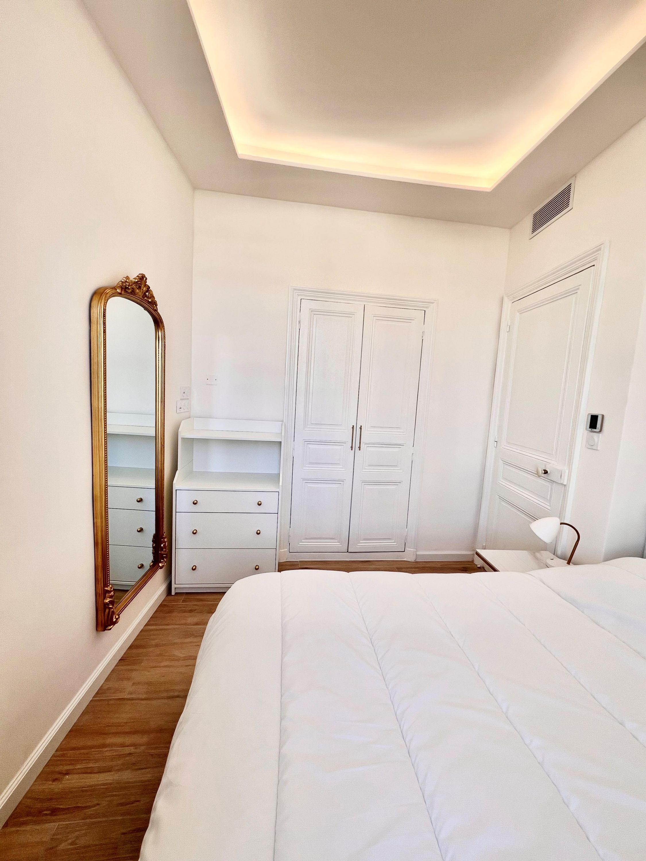 Un dormitorio con cama, armario, cómoda y espejo.
