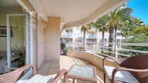 En balkon med fletmøbler, et glasbord og udsigt til palmer og bygninger.