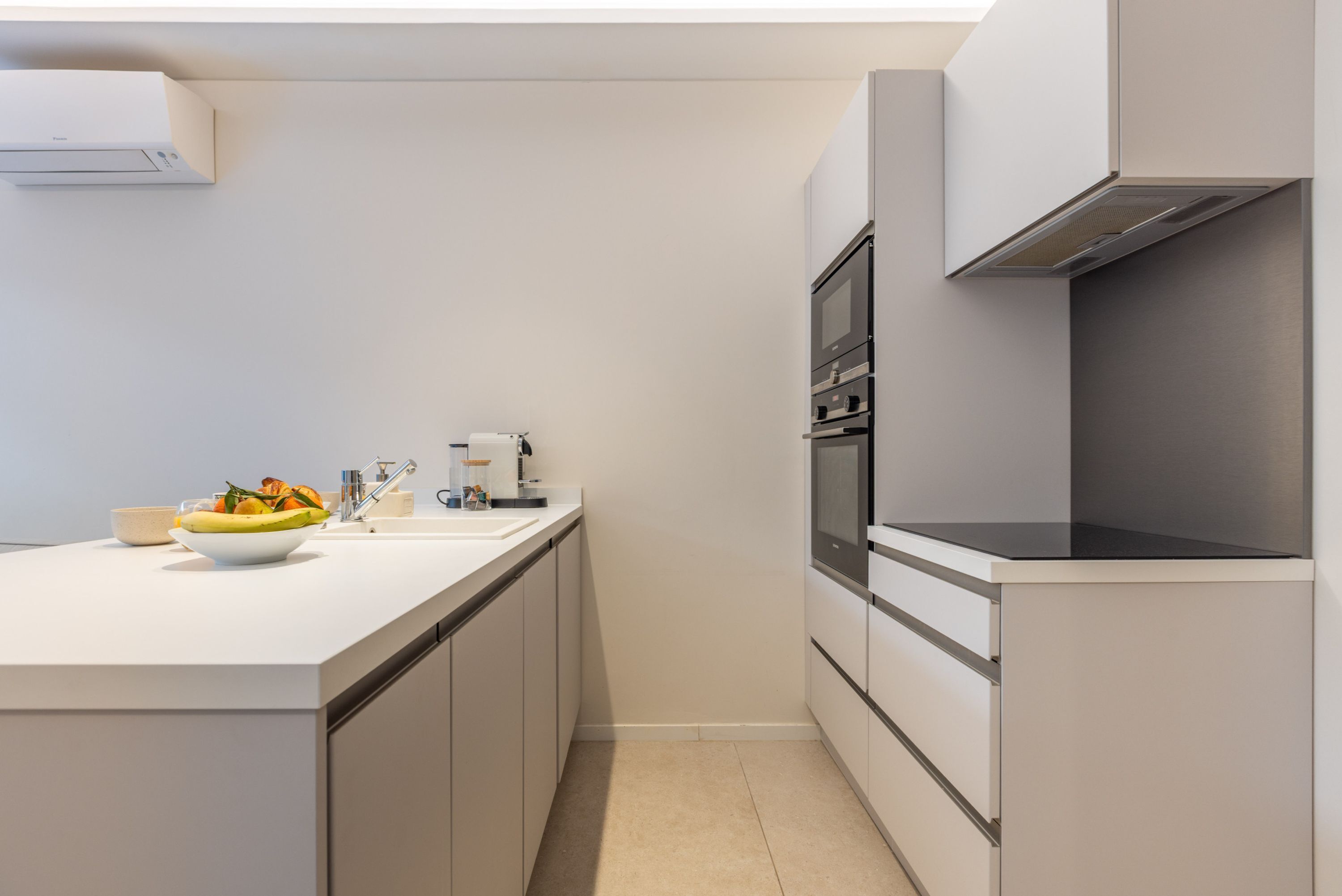 Een moderne keuken met een wit aanrecht, een inbouwoven en een roestvrijstalen afzuigkap.