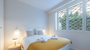 A bedroom with a bed, bedside lamps, a window with a view, and a small round ottoman. - 2 Chambres-terrasse-pointe Croisette A2b267 (Cannes)