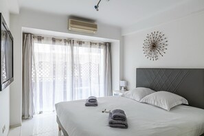 Ein Hotelzimmer mit einem großen Bett, einem Kopfteil, einer Wandklimaanlage, einem Fenster mit durchsichtigen Vorhängen und einem dekorativen Wandbild.