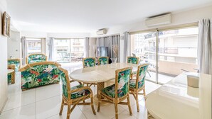 Ein Essbereich mit einem runden Tisch, Korbstühlen, großen Fenstern und einem Balkon.