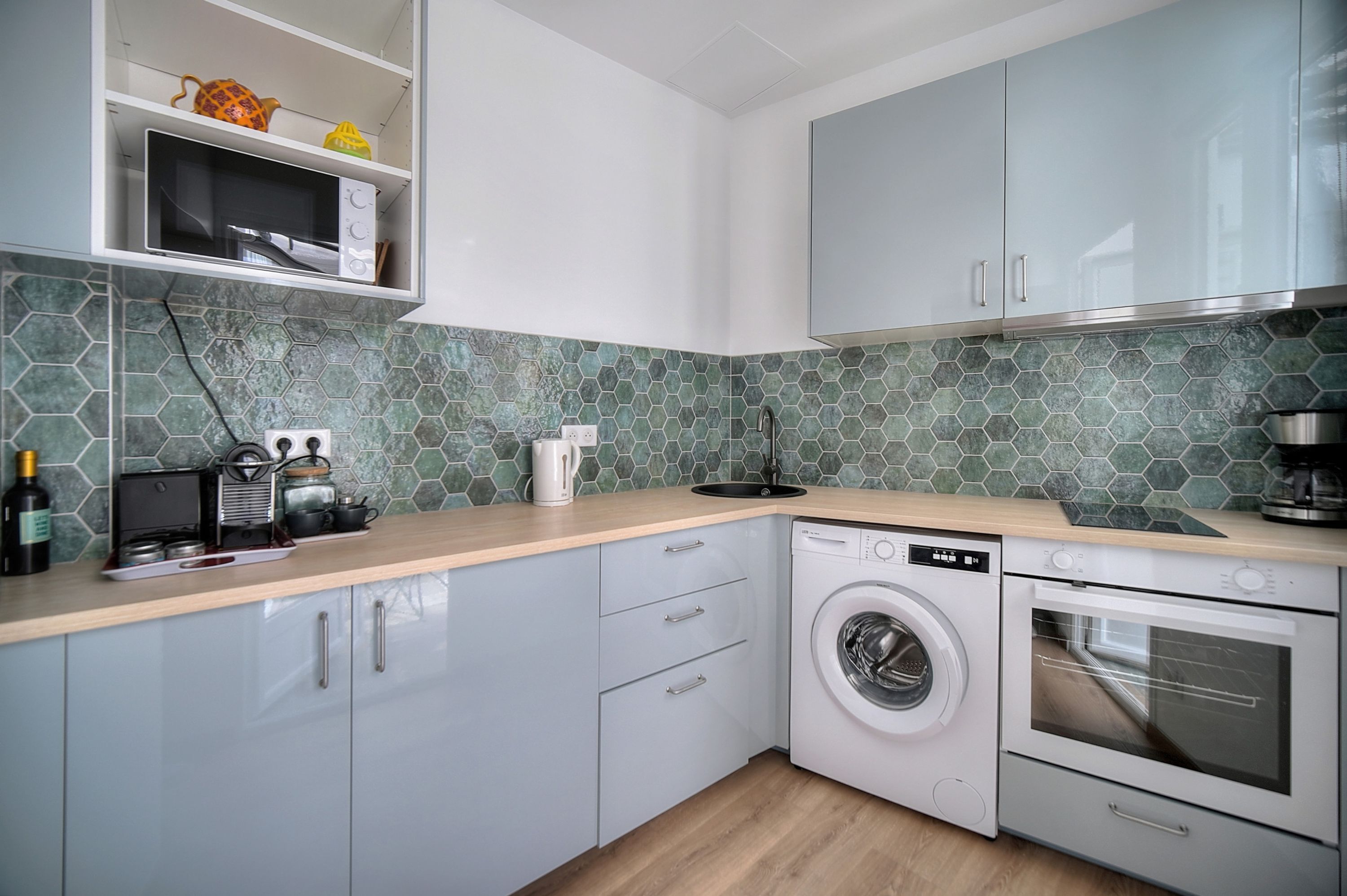 Una cocina moderna con lavadora, horno, microondas y cafetera sobre la encimera.