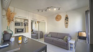 Una sala de estar moderna con un sofá gris, una mesa de comedor y una zona de cocina con electrodomésticos.