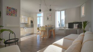 A modern living room with a sofa, a dining area with stools, a kitchen, and a TV. - Maison DE Ville 6 Chambres Terrasse A6b002 (Cannes)