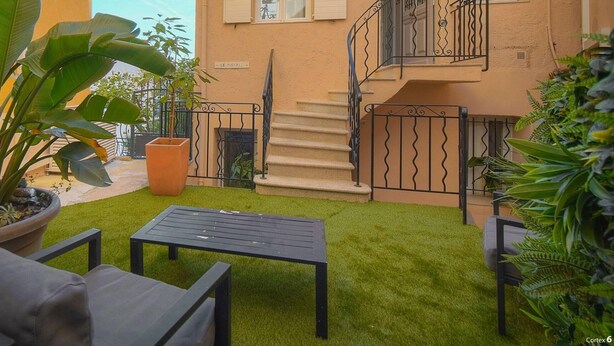 A courtyard with artificial grass, a seating area with a table and chairs, potted plants, and a staircase leading to an upper floor. - Maison DE Ville 6 Chambres Terrasse A6b002 (Cannes)