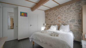 A bedroom with a stone wall, a bed with white linens, and a door with a colorful artwork. - Maison DE Ville 6 Chambres Terrasse A6b002 (Cannes)