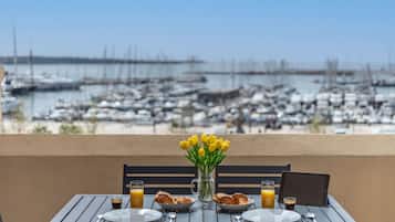 Una mesa de comedor con platos, cubiertos y un jarrón de flores amarillas, con vista a un puerto deportivo y barcos.
