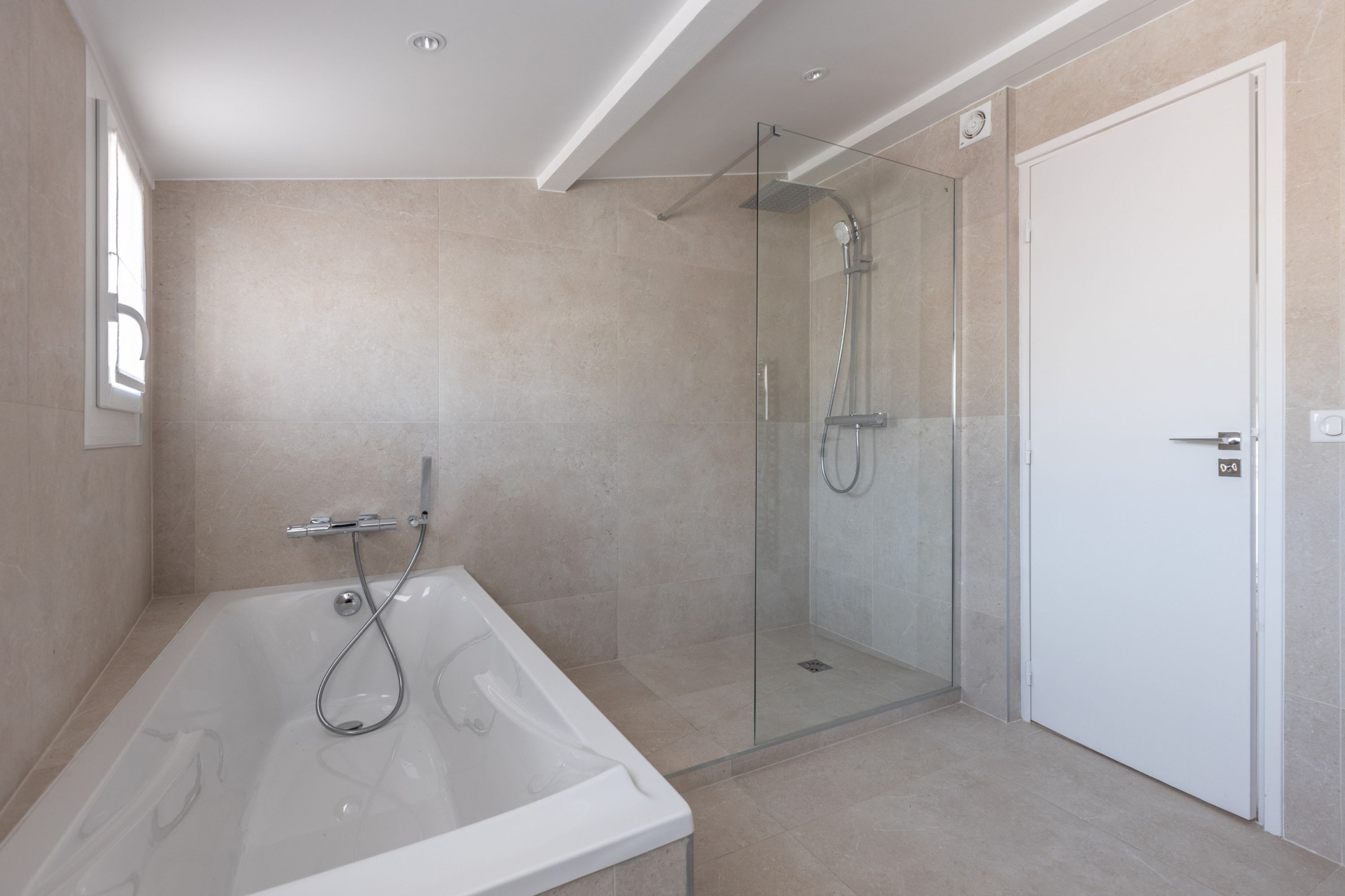 Une salle de bain moderne avec une douche à parois de verre, une baignoire sur pieds et une porte blanche.