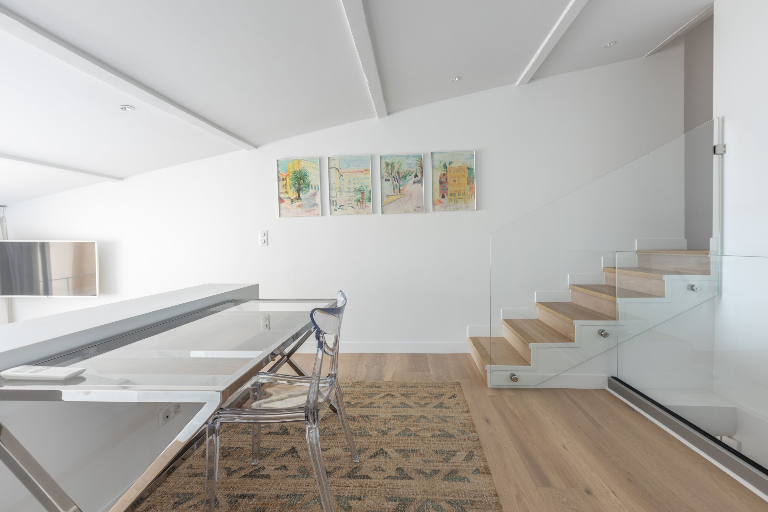 A modern interior with a glass staircase, a dining area with a glass table and chairs, and three artworks on the wall.