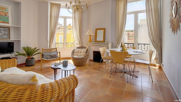 A living room with a TV, wicker furniture, a fireplace, and a balcony with curtains. - Lumineux 3 Pieces Dans LE Carre D OR A2b196 (Cannes)