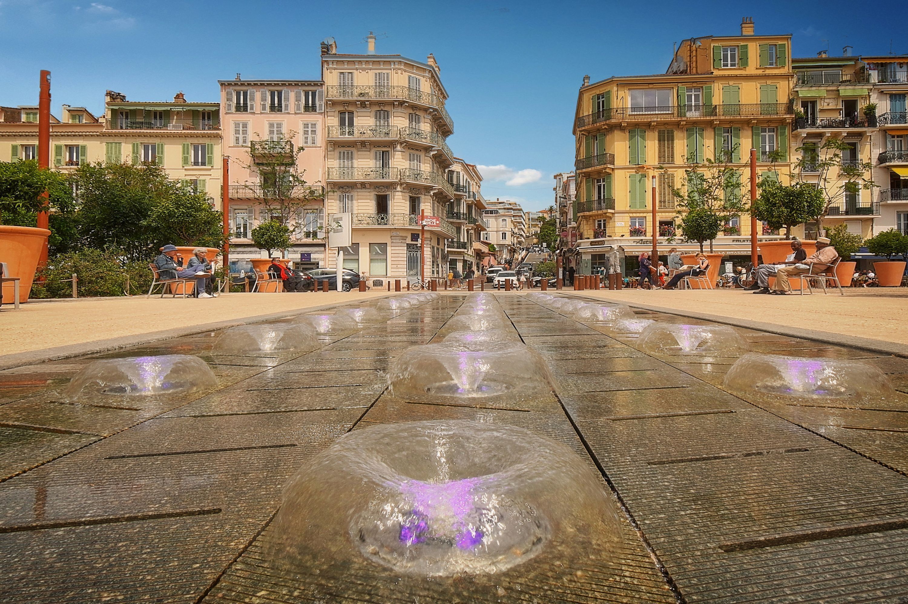 Une place publique agrémentée d’une fontaine, bordée de bâtiments historiques et dotée d’espaces de repos en plein air.