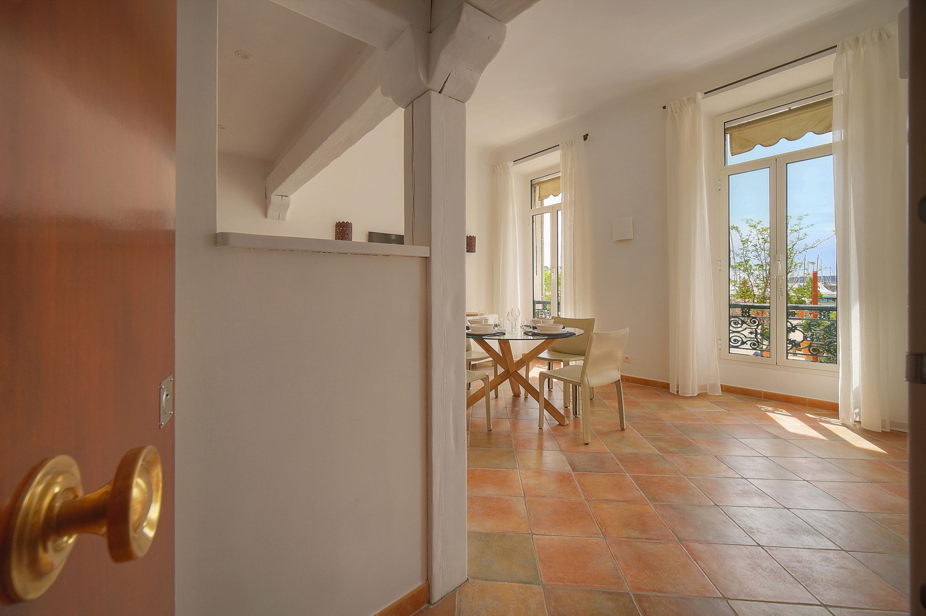 A room with a dining area, a large window with curtains, and a tiled floor.
