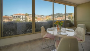 A dining area with a table set for two, large windows offering a city view, and a small table with flowers. - Ref 670723 in Cannes (Cannes)