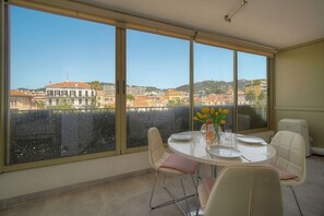 Ein Essbereich mit Tisch für zwei Personen, große Fenster mit Blick auf die Stadt und ein kleiner Tisch mit Blumen.