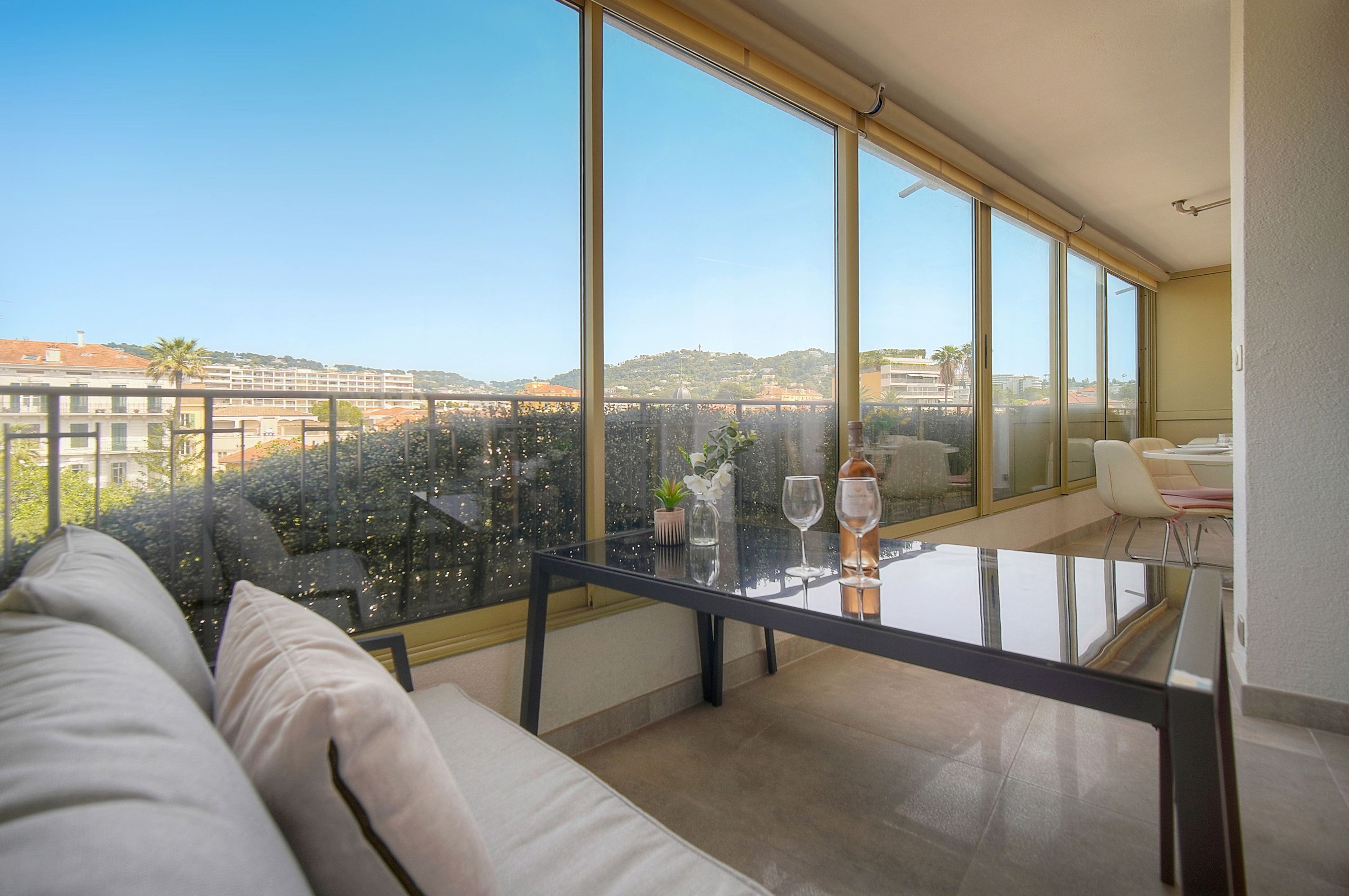 Un balcon avec une table en verre, un canapé blanc et une vue dégagée sur le paysage urbain.