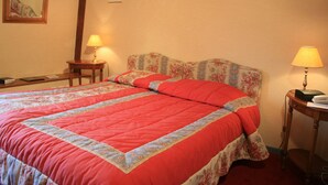 Un lit bien fait, recouvert d’une couette rouge et bleue, deux tables de chevet avec des lampes et une tête de lit à motifs floraux.