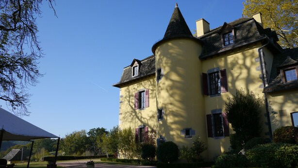 Un grand bâtiment jaune, doté d’une tourelle et de nombreuses fenêtres, entouré de verdure.