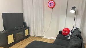 Ein modernes Wohnzimmer mit einem schwarzen Sofa, einem Flachbildfernseher, einer kleinen Kommode und einer Wanduhr.
