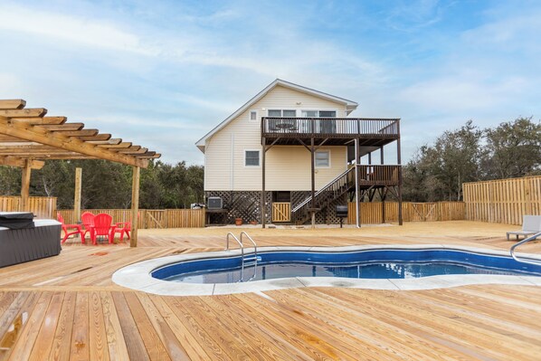 En træterrasse med swimmingpool, en overdækket patio og et toetagers hus med balkon.