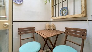 Ein kleiner Holztisch mit zwei Stühlen, ein Fenster mit Metallgitter und dekorative Teller an der Wand.