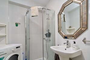 A modern bathroom with a glass-enclosed shower, a white sink, a mirror with a decorative frame, and a washing machine. - Holiday Home 'De Tio' with Private Terrace, Wi-Fi and Air Conditioning (Torre del Mar)