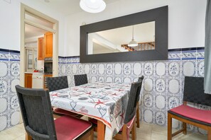A dining area with a table set for four, surrounded by chairs with red cushions. A large mirror hangs above the table, and the walls are decorated with blue and white patterned tiles. - Holiday Home 'De Tio' with Private Terrace, Wi-Fi and Air Conditioning (Torre del Mar)