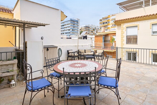 A patio with a round table and chairs, a white building, and a multi-story residential building in the background. - Holiday Home 'De Tio' with Private Terrace, Wi-Fi and Air Conditioning (Torre del Mar)