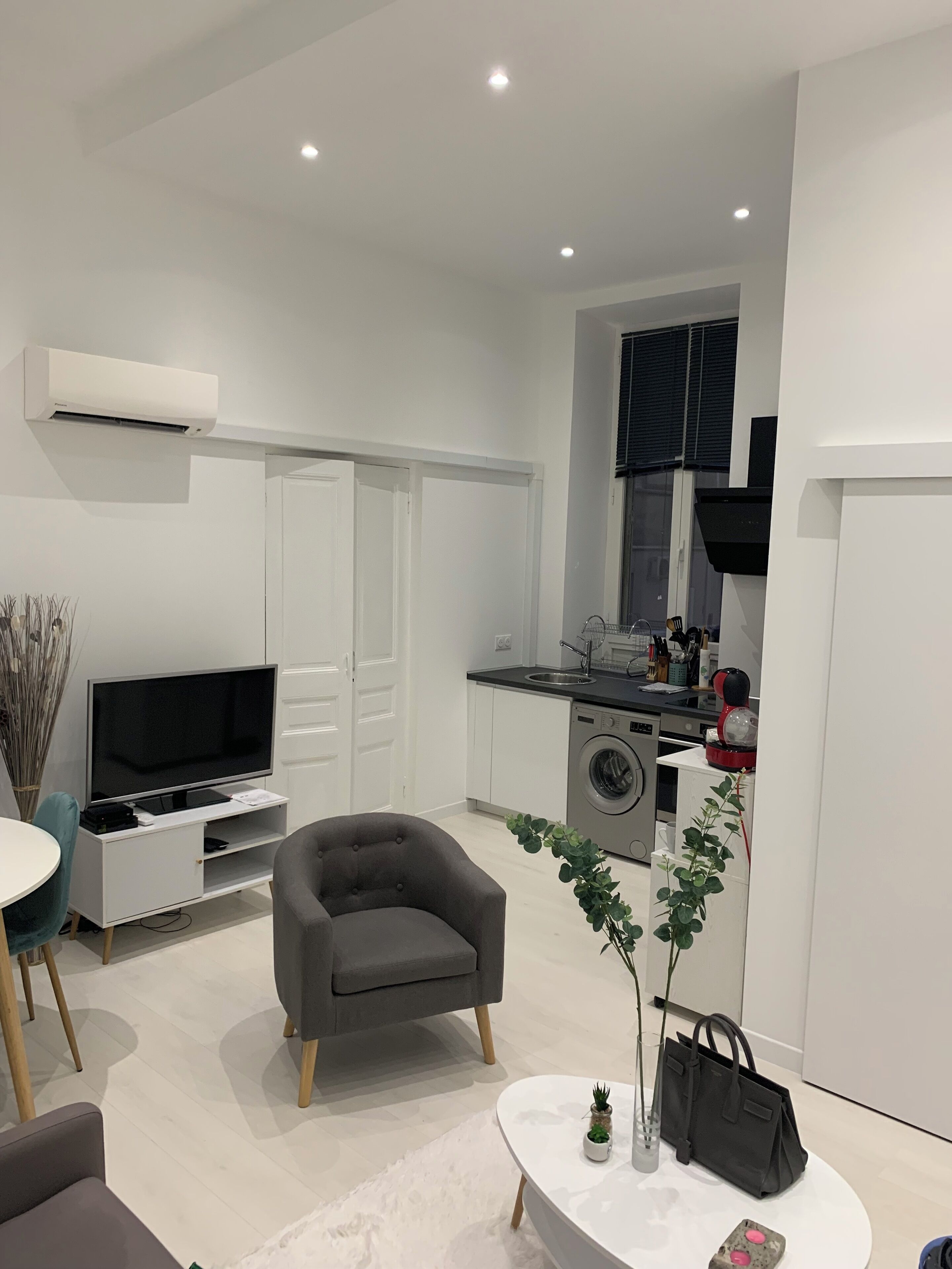 Un salon moderne avec un fauteuil gris, un téléviseur à écran plat et un coin repas comprenant une table et des chaises.