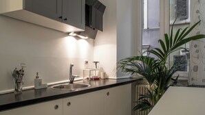 A modern kitchen with a black countertop, stainless steel sink, and grey cabinets. - Intrà residenza in trastevere (Rome)
