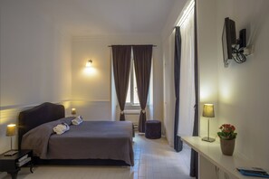 A hotel room with a bed, bedside lamps, a desk with a plant, and a television. - Intrà residenza in trastevere (Rome)