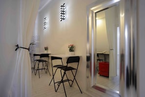 Un couloir étroit avec une porte blanche, une petite table entourée de chaises, un buffet rouge et une plante en pot.