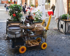 Un chariot de vendeur ambulant équipé pour la préparation de plats et proposant divers aliments, entouré de tables et de chaises en plein air, ainsi que de plantes en pot.