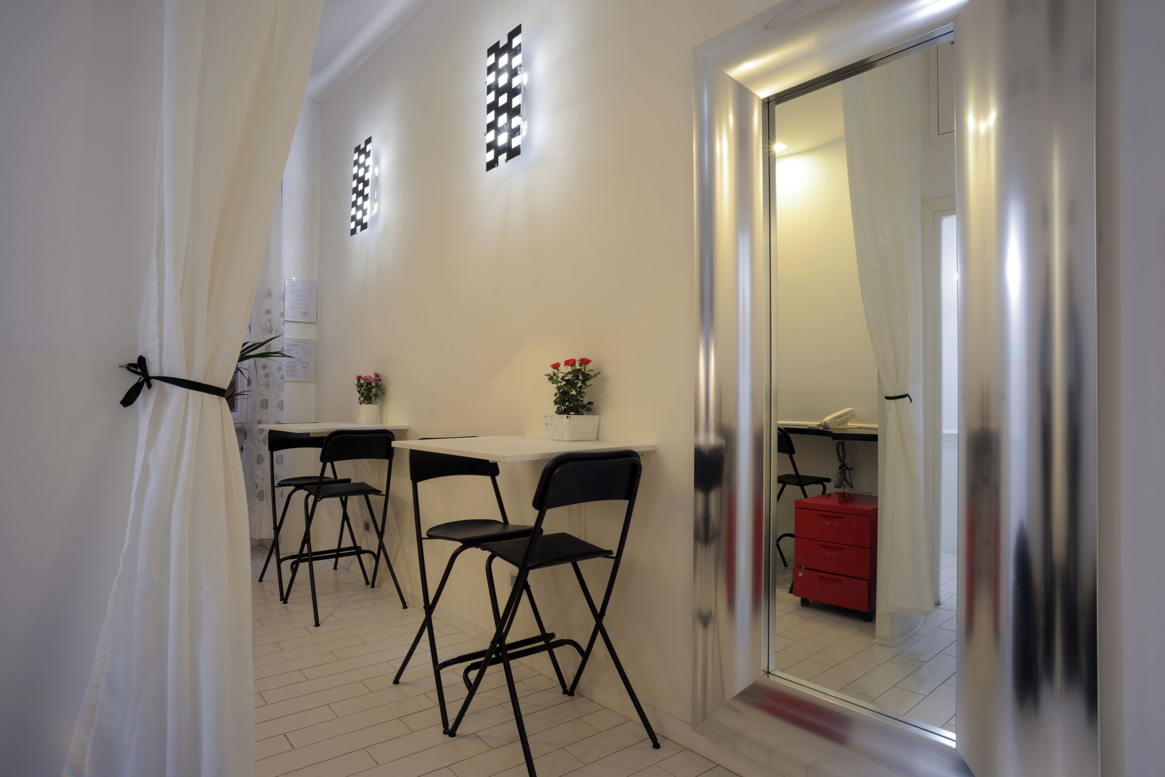 A room with a white wall, a black folding chair, a small table, a potted plant, and a red cabinet.