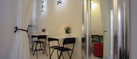 A room with a white wall, a black folding chair, a small table, a potted plant, and a red cabinet.