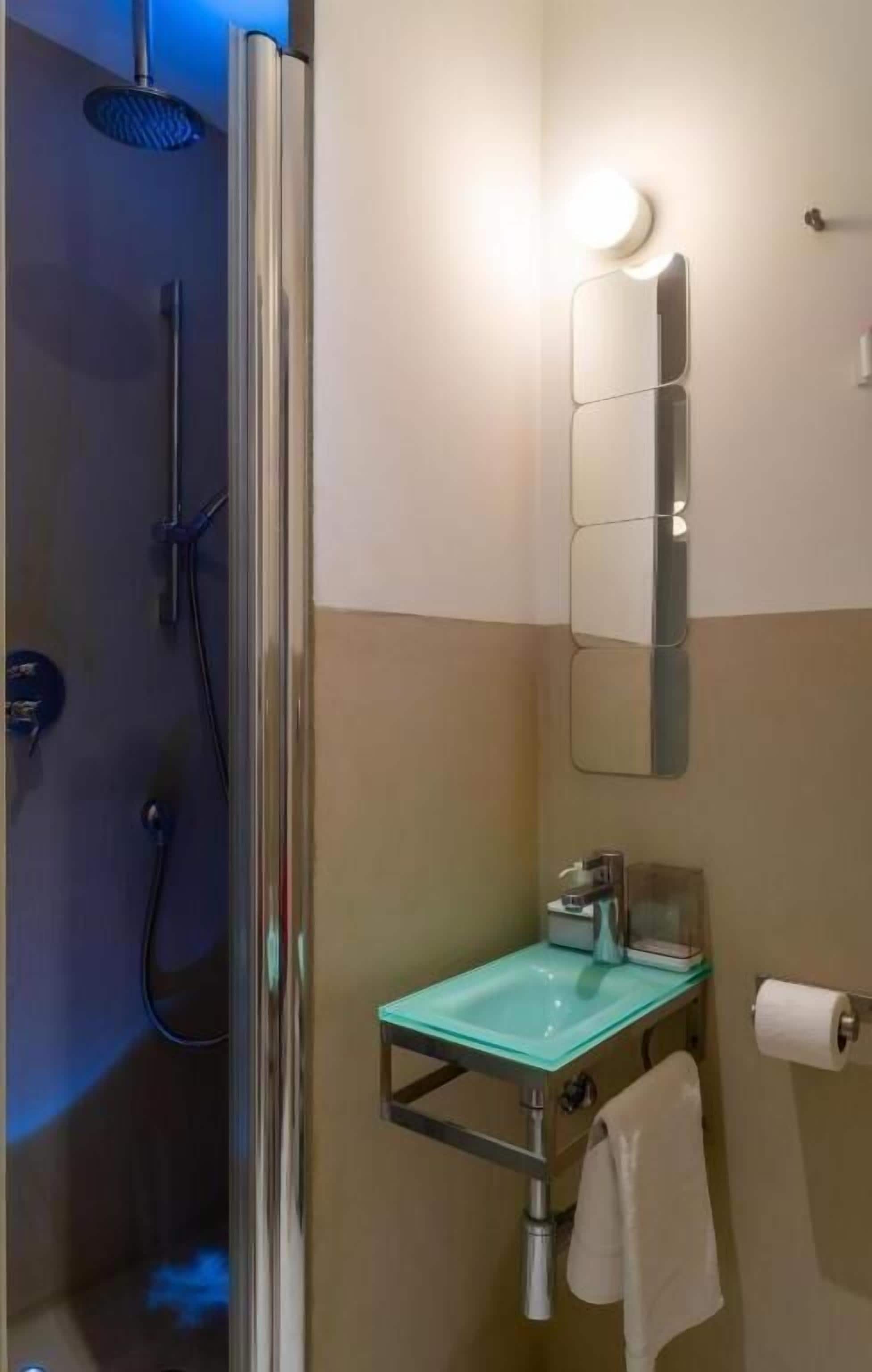 Ein modernes Badezimmer mit einem Waschbecken aus Glas, einer Duschbrause, einem wandmontierten Spiegel und einem Handtuchhalter.