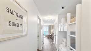 Un couloir orné d’une affiche encadrée sur laquelle on peut lire « Eau salée + couchers de soleil », qui mène à une pièce comprenant un lit et un bureau.