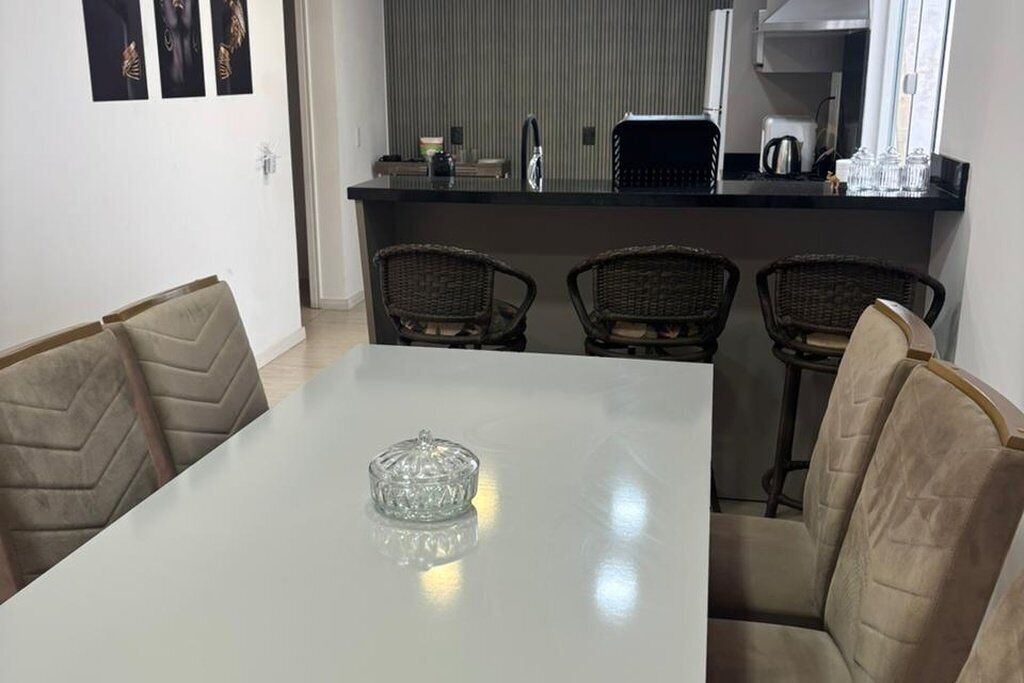 A dining area with a white table, four wicker chairs, and a kitchen in the background.