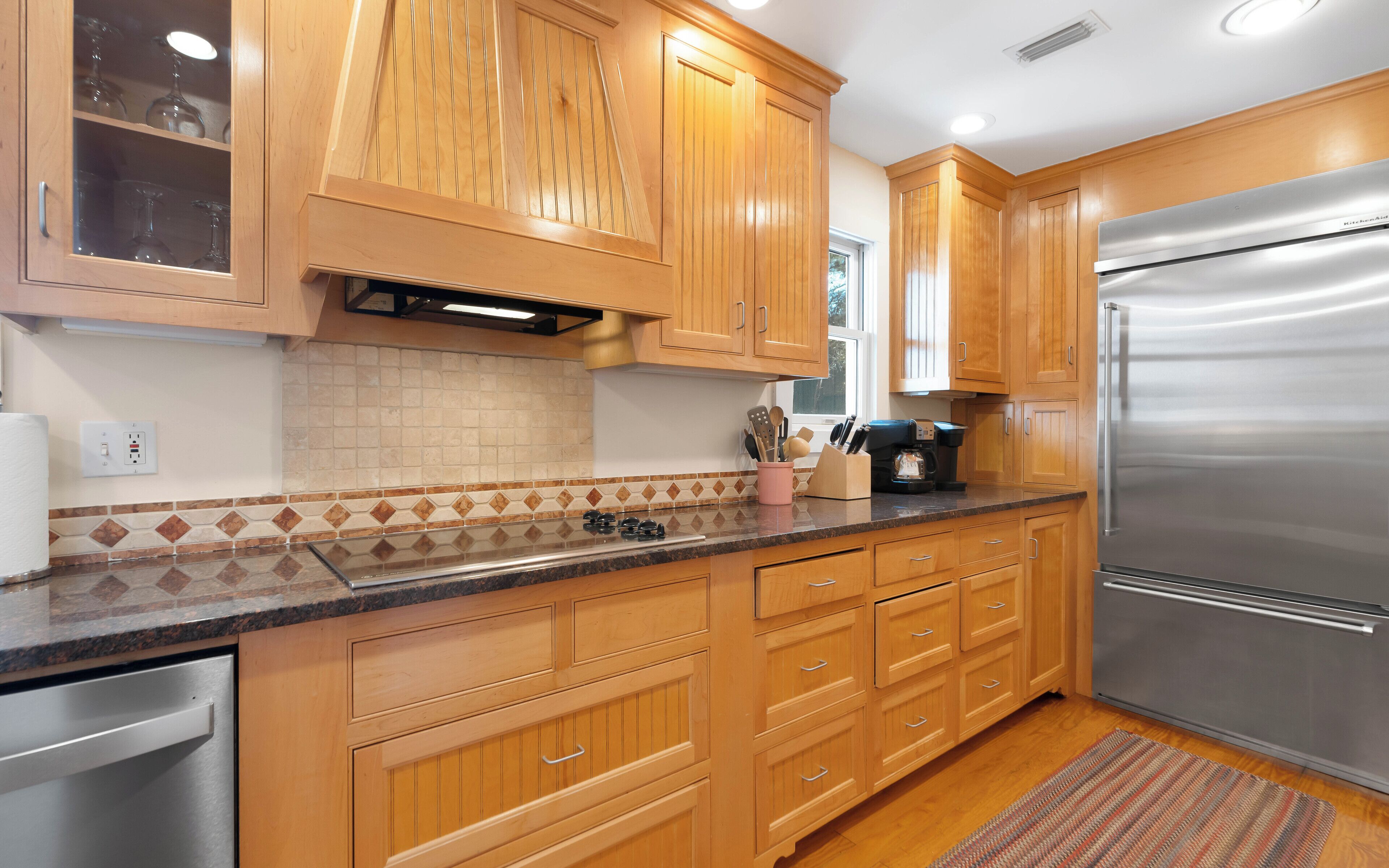 A kitchen with wooden cabinets, a stainless steel refrigerator, a coffee maker, and a tiled backsplash.