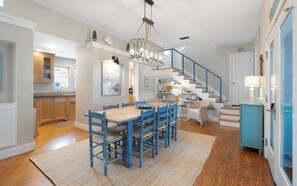 A spacious kitchen with wooden cabinets, a dining area with blue chairs, and a staircase with blue railings. - Son Worshipers - Seaside Home near Iconic Town Council! (Santa Rosa Beach)