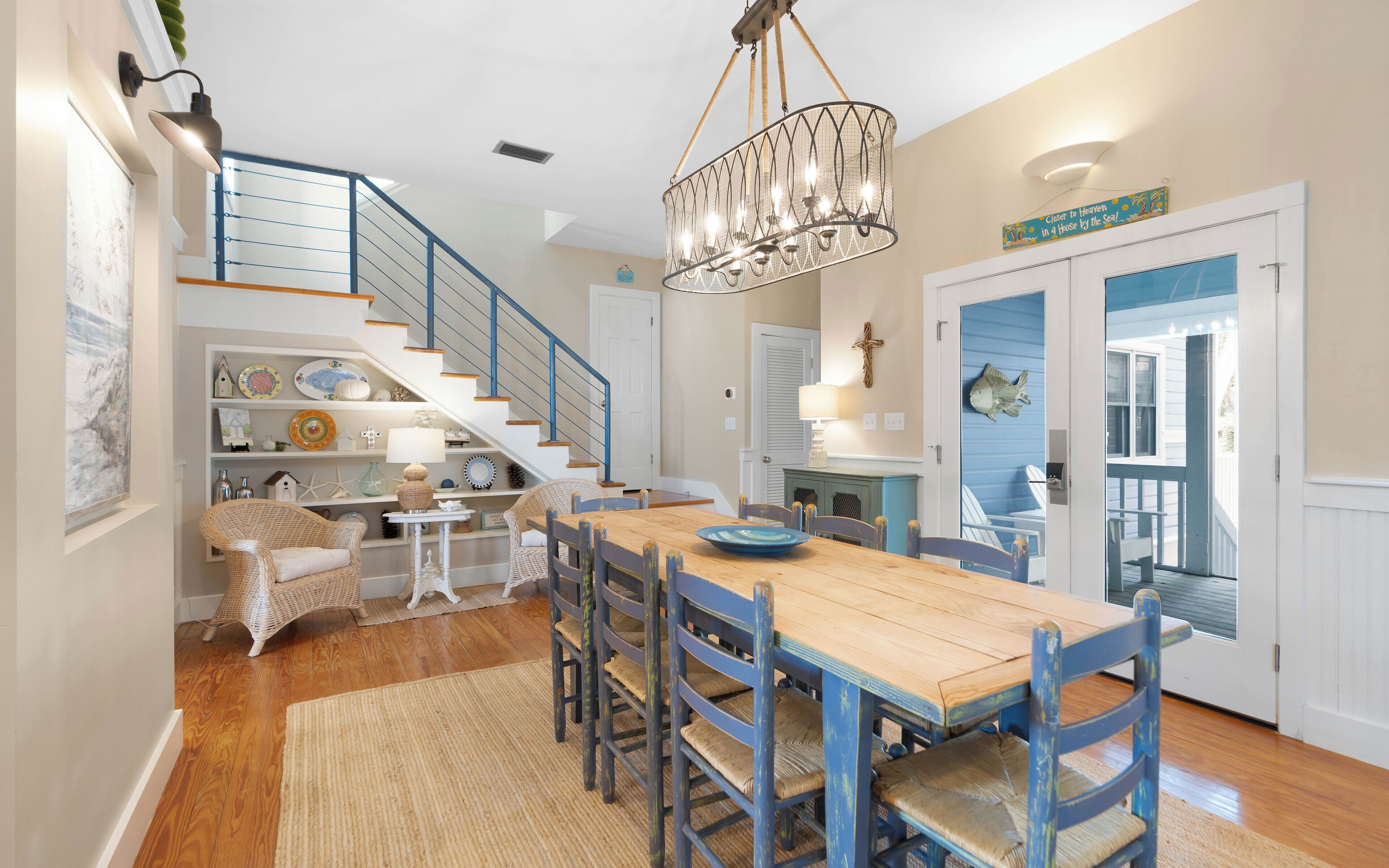A dining area with a wooden table and blue chairs, a staircase with blue railings, and a chandelier.