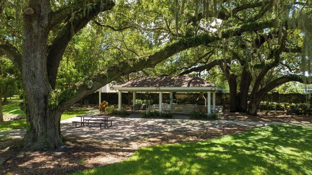 Um gazebo com cobertura, rodeado por árvores grandes e uma mesa de piquenique.