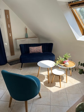 Una sala de estar moderna con un sofá azul oscuro, un sillón verde azulado y una pequeña mesa blanca con plantas en macetas.