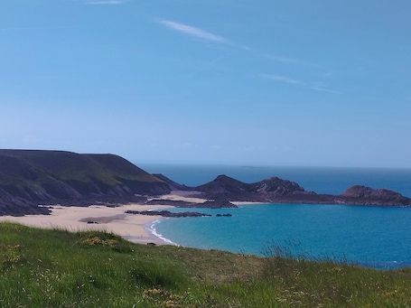 A coastal landscape with a beach, grassy areas, and rocky outcrops.. Studio "Le Petit Cocon" near the sea