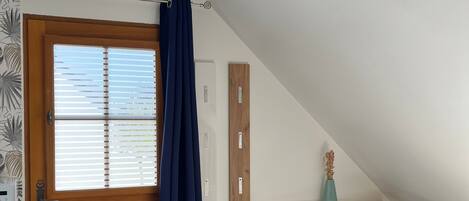 A room with a wooden door, a blue curtain, a blue sofa with a floral pillow, a white radiator, and a wooden shelf with a vase.