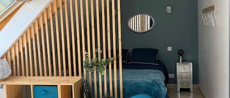 Un dormitorio moderno con techo inclinado, una cama, un escritorio con espacio de almacenamiento, una silla, un televisor y una mesita de noche.