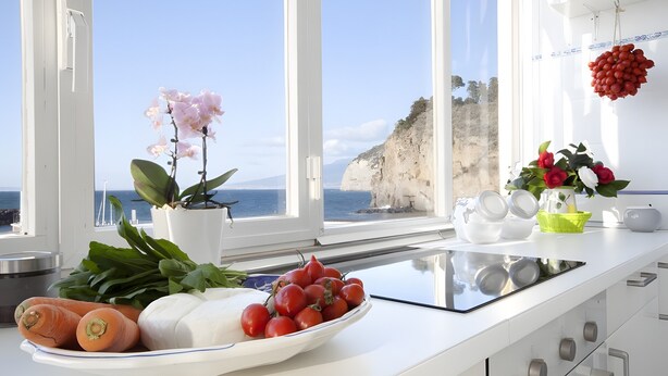 Una cocina con vista al mar, una orquídea en maceta y un bol de tomates.