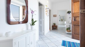Un pasillo con suelo de baldosas blancas, una puerta de madera, un armario blanco con espejo y una orquídea en maceta.