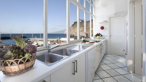 Una cocina con vista al mar, armarios blancos, un fregadero y una cesta de verduras.